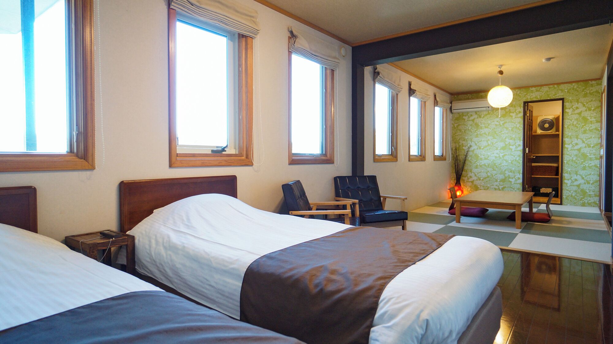 A hotel room with two beds, a chair, a table, and a bathroom visible through an open door.