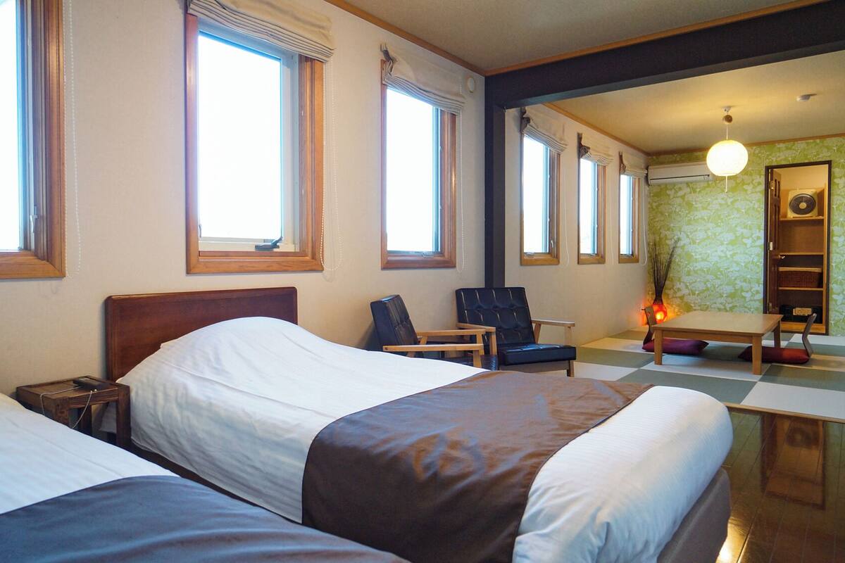 Ein Hotelzimmer mit zwei Betten, einem Sessel, einem Tisch und einem durchgegangenen Tür sichtbaren Badezimmer.