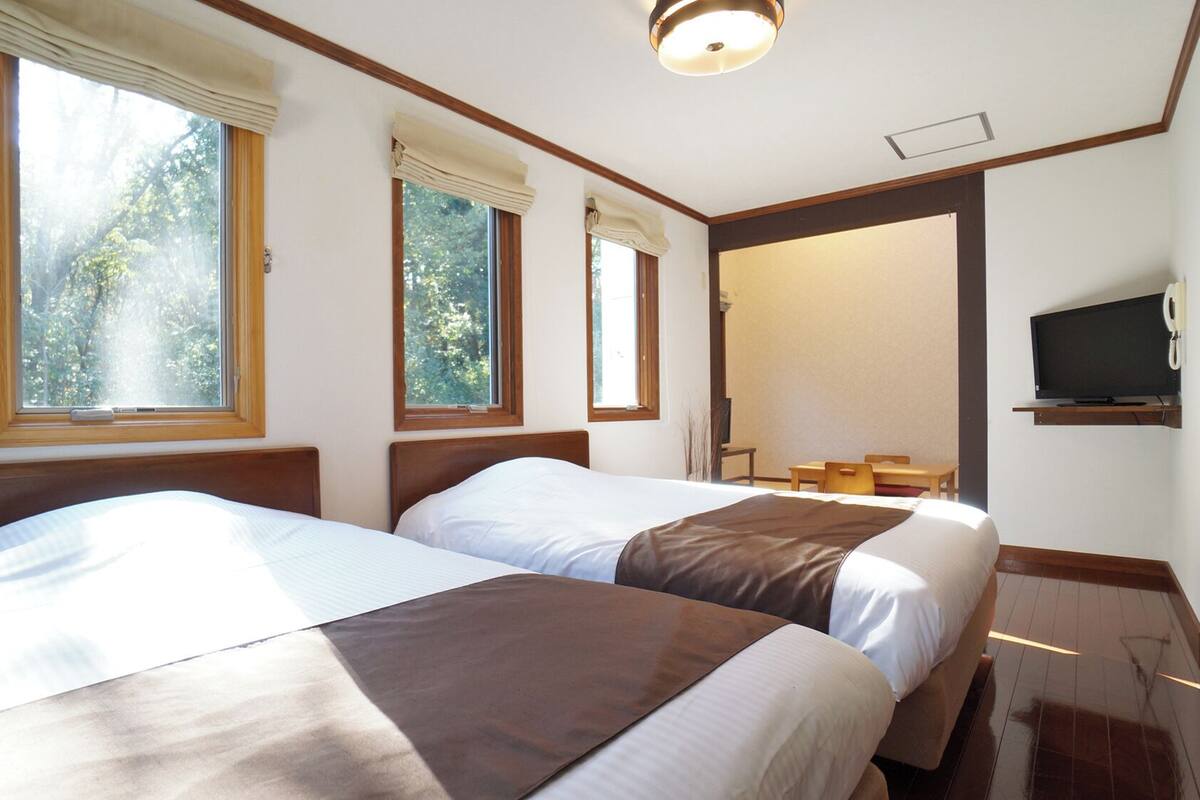 Ein Hotelzimmer mit zwei Betten, einem Fernseher und einem Fenster mit Blick auf Bäume.