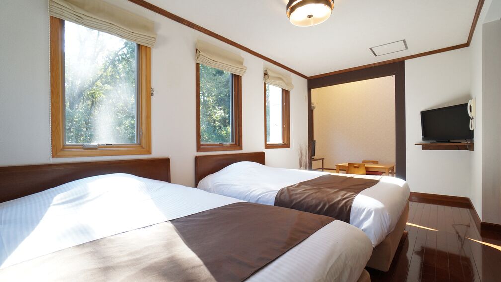 A hotel room with two beds, a television, and a window with curtains.