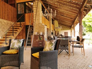 Un espace extérieur aménagé avec des meubles en osier, protégé par un auvent, comprenant un escalier et un lustre.