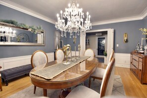 A dining room with a large oval table, chairs, a chandelier, and a mirror on the wall.