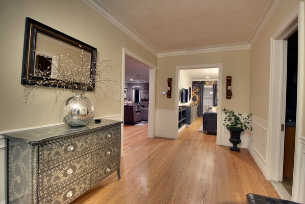A hallway with a wooden floor, a decorative dresser, a mirror, and a vase with branches.