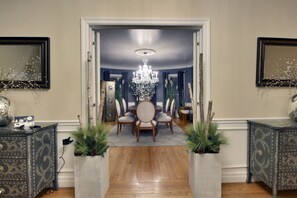 Un coin repas agrémenté d’un lustre, d’une table ronde et de chaises. Des plantes décoratives et un miroir ornent les murs.