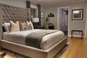 A bedroom with a tufted headboard, a bed with multiple pillows, a bedside table with a lamp, and a small side table with a plant.