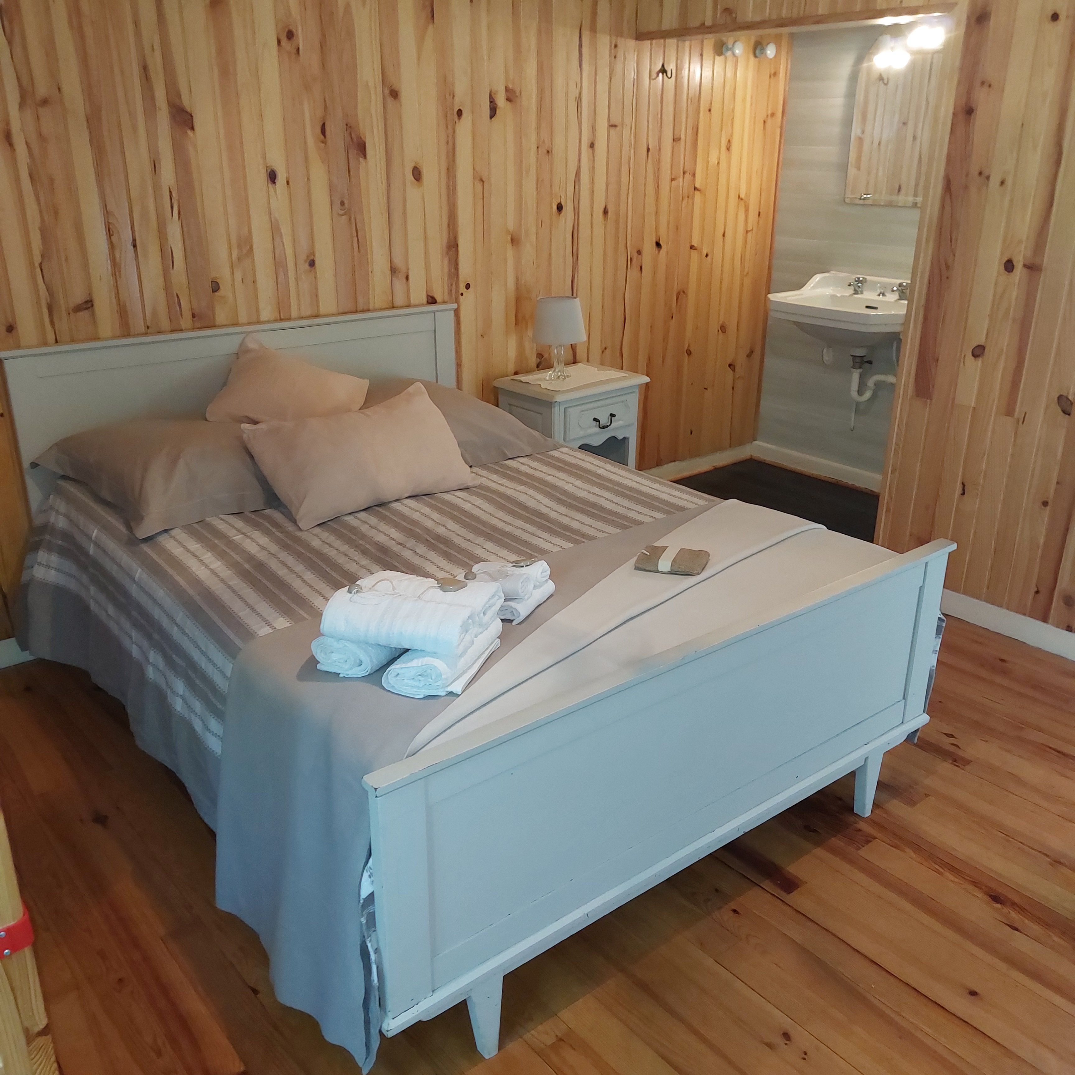 Une pièce aux murs lambrissés, comprenant un lit, une table de chevet, une lampe et une salle de bain avec un lavabo.