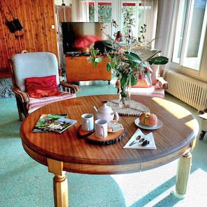 Un salon chaleureux avec une table basse en bois, un fauteuil confortable, un téléviseur et une plante en pot.