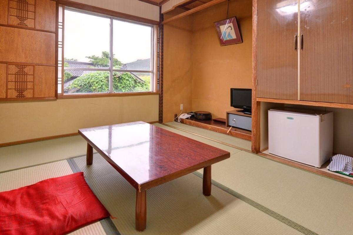 Una habitación japonesa tradicional con suelo de tatami, una mesa de madera baja, un televisor y un refrigerador.