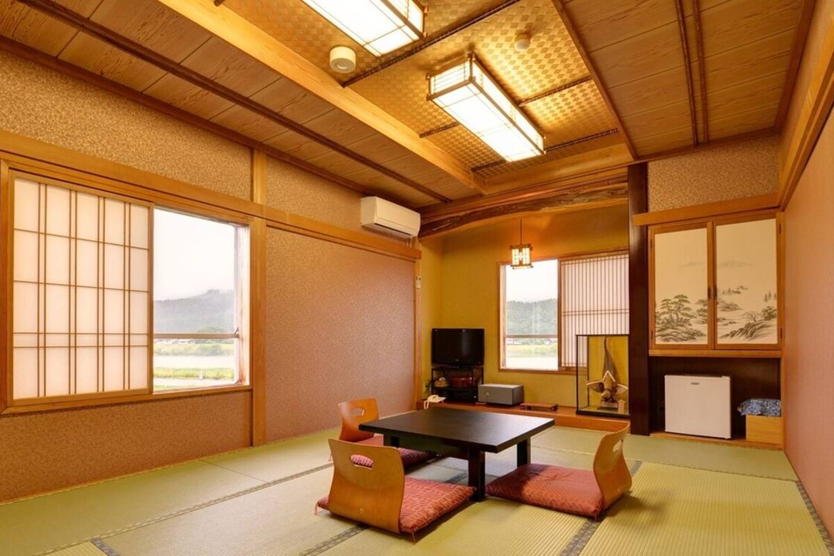 Una habitación japonesa tradicional con suelo de tatami, una mesa baja, cojines, puertas correderas y vistas al exterior.