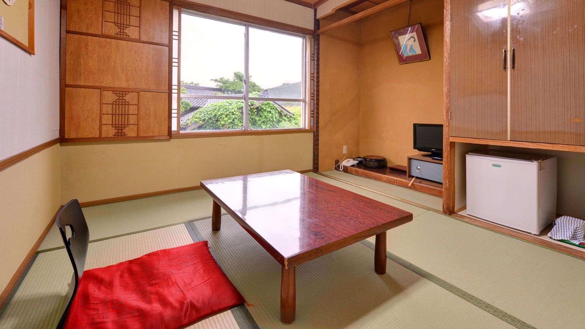 Ein traditioneller japanischer Raum mit Tatami-Böden, einem niedrigen Tisch, einem Stuhl, einem Fernseher und einem Kühlschrank.