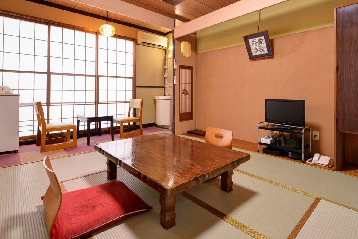 Una habitación japonesa tradicional con suelo de tatami, una mesa de madera, un televisor y un refrigerador.
