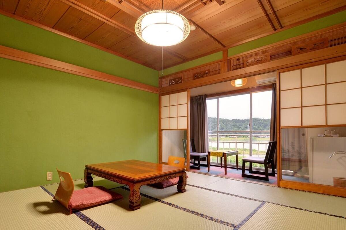 Una habitación tradicional japonesa con suelo de tatami, una mesa de madera y puertas correderas que dan a un balcón.