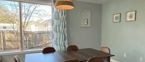 A dining room with a table and chairs, a hanging light fixture, and a view of the outside.