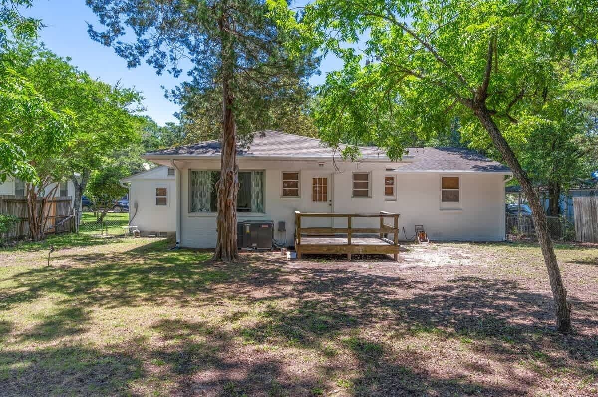 A single-story house with a front porch, a small deck, and a yard with trees.