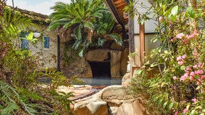 A stone archway leading to a cave-like entrance, surrounded by lush greenery and a small pond. - Gyokusenkan (Ebino)