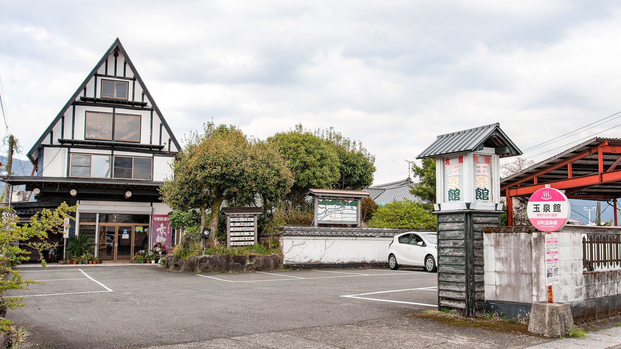 A traditional Japanese building with a sloped roof, a parking lot, and a sign indicating a restaurant.