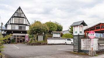 A traditional Japanese building with a sloped roof, a parking lot, and a sign indicating a restaurant.