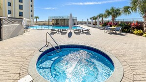 A swimming pool area with a hot tub, lounge chairs, and a covered seating area.