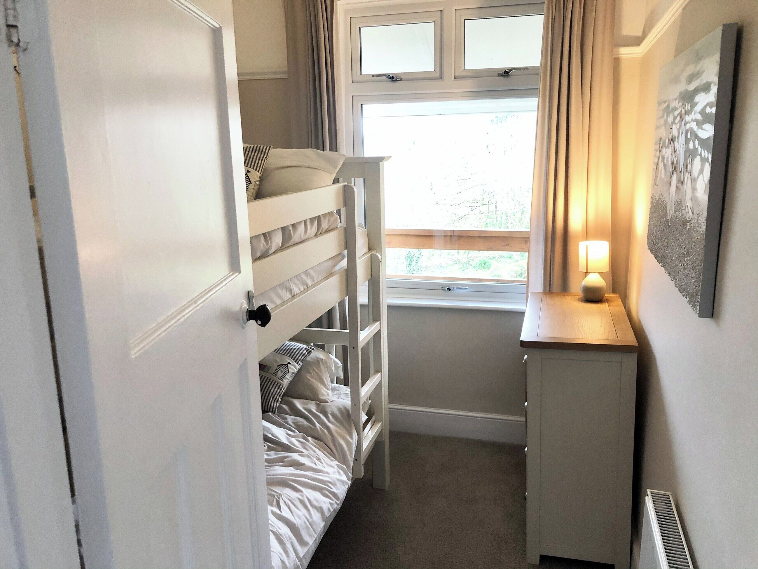 Een compacte slaapkamer met een stapelbed, een klein bureau, een raam met gordijnen en een radiator.
