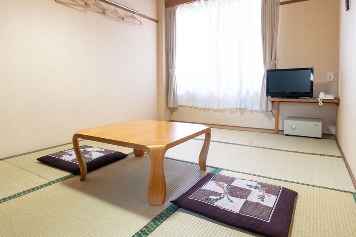 Una habitación con suelo de tatami, una mesa de madera, un televisor y un mueble pequeño.