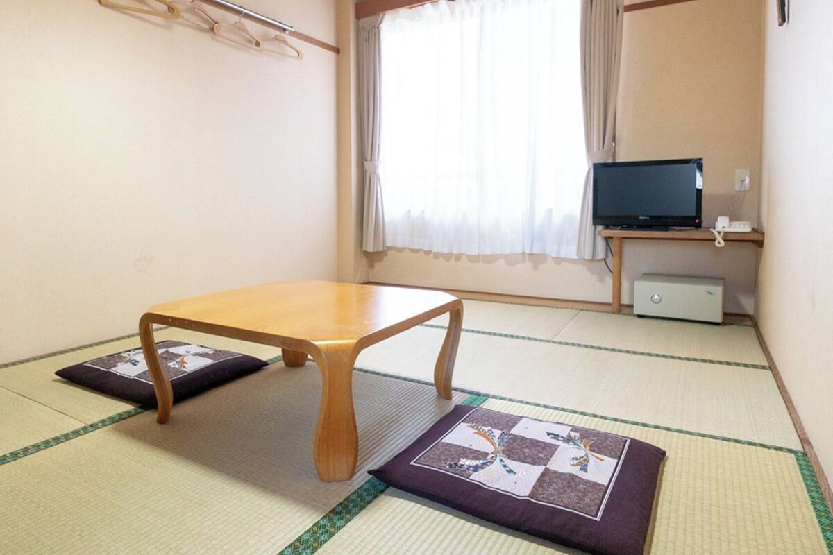 Una habitación con suelo de tatami, una mesa de madera, un televisor y un mueble bajo.