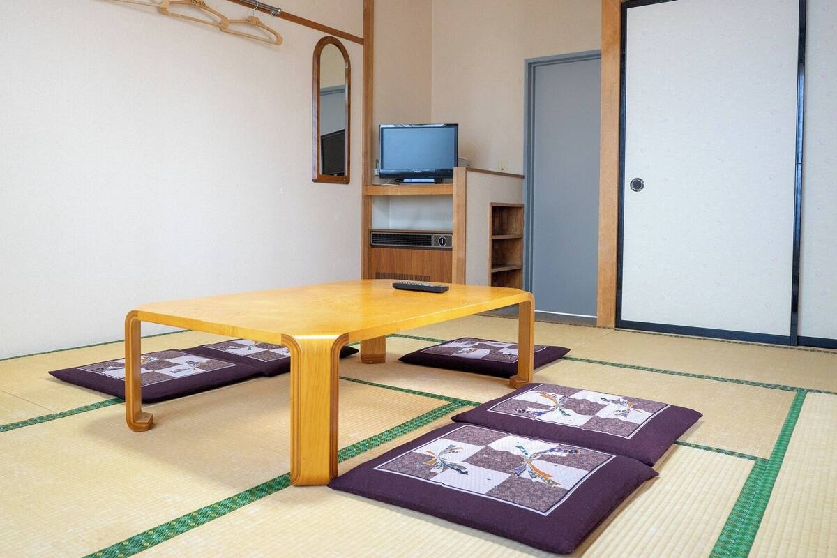 Una habitación con esteras de tatami, una mesa de madera, un televisor y un armario.