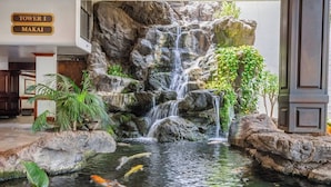 A waterfall feature with koi fish, surrounded by rocks and plants, and a sign indicating 'Tower I Makai'. - Waikiki Banyan condo w/ beach access & pool (Honolulu)