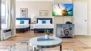 A hotel room with a bed, a TV, a bedside table, a small plant, and a glass coffee table. - Waikiki Banyan condo w/ beach access & pool (Honolulu)