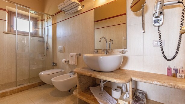 A bathroom with a glass-enclosed shower, a bidet, a sink with a mirror, and a hairdryer mounted on the wall. - LE BUCHE ESTATE  VILLA RENTAL  (Sarteano)