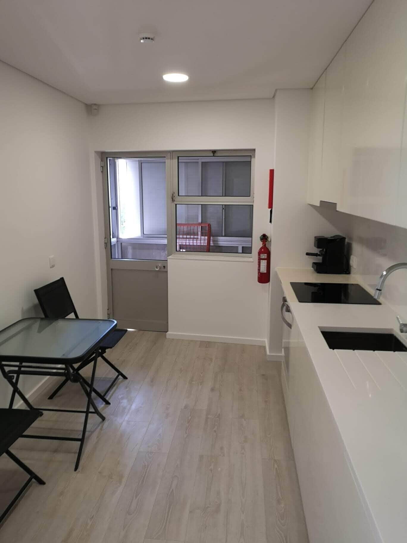 A compact kitchen with a dining table and chairs, a window, and a fire extinguisher.