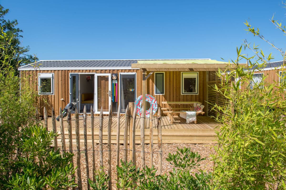 Una casa móvil de madera con terraza, mesa de billar y flotador de piscina.