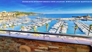 A marina with numerous boats docked, a stone wall in the foreground, and a coastal town in the background. - Seafront rental by Thierry Bourgait (Banyuls-sur-Mer)