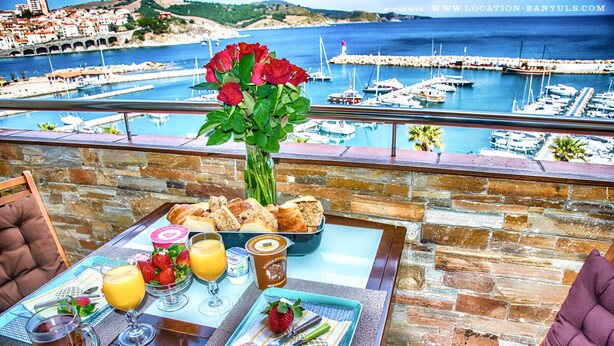 A breakfast table with pastries, a fruit bowl, a glass of orange juice, and a vase of red roses. - Seafront rental by Thierry Bourgait (Banyuls-sur-Mer)