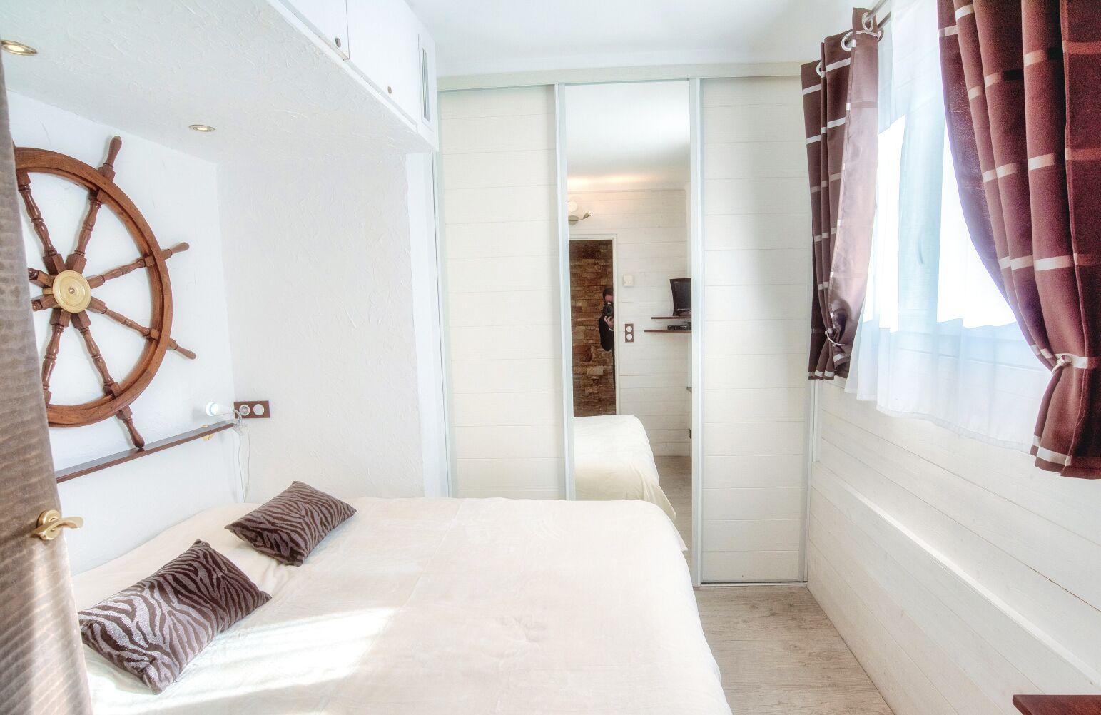 A bedroom with a bed, a wooden ship's wheel decoration, a sliding door, and a window with curtains.