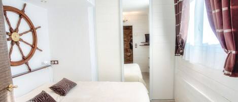 A bedroom with a bed, a wooden ship's wheel decoration, a sliding door, and a window with curtains.