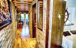 A hallway with wooden flooring and stone walls, leading to a bedroom with a bed and a ship's wheel on the wall. - Seafront rental by Thierry Bourgait (Banyuls-sur-Mer)