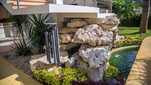 A modern outdoor area with a stone structure, a small pond, and a metal sculpture. - AZCAPRI® Villa Boutique & Spa -Queen-  NEW! (Alfredo V. Bonfil)
