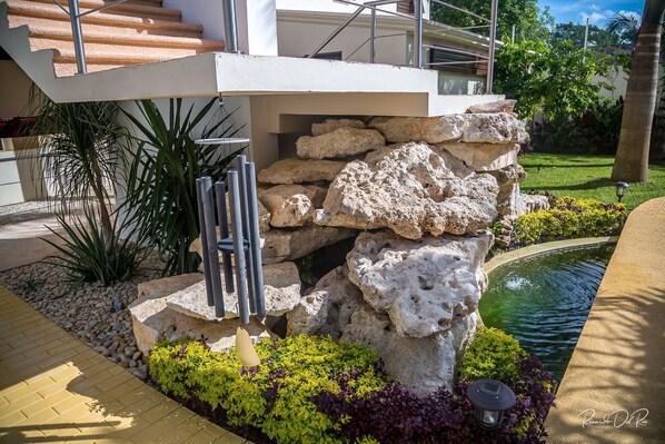 A modern outdoor area with a stone structure, a small pond, and a metal sculpture.
