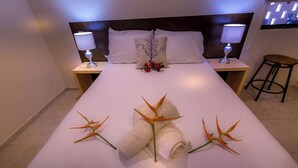 A neatly made bed with white linens, two bedside lamps, a small table with a chair, and a decorative arrangement of flowers and a rolled towel on the bed. - AZCAPRI® Villa Boutique & Spa -Queen-  NEW! (Alfredo V. Bonfil)