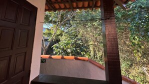 A balcony with terracotta tiles, a wooden door, and a view of greenery. - Suíte em Geribá, Próximo a Praia (Armação do Búzios)