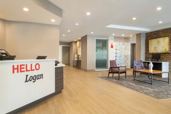 Un área de recepción con un cartel que dice 'HELLO Logan', un mostrador de recepción, dos sillas, una mesa y una pared con un cuadro abstracto y colorido.
