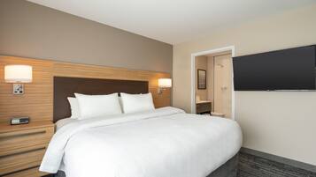 A hotel room with a large bed, bedside lamps, a flat-screen TV, and a wooden headboard.