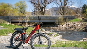 Ein rotes Fahrrad steht an einem Fluss, im Hintergrund eine Brücke.
