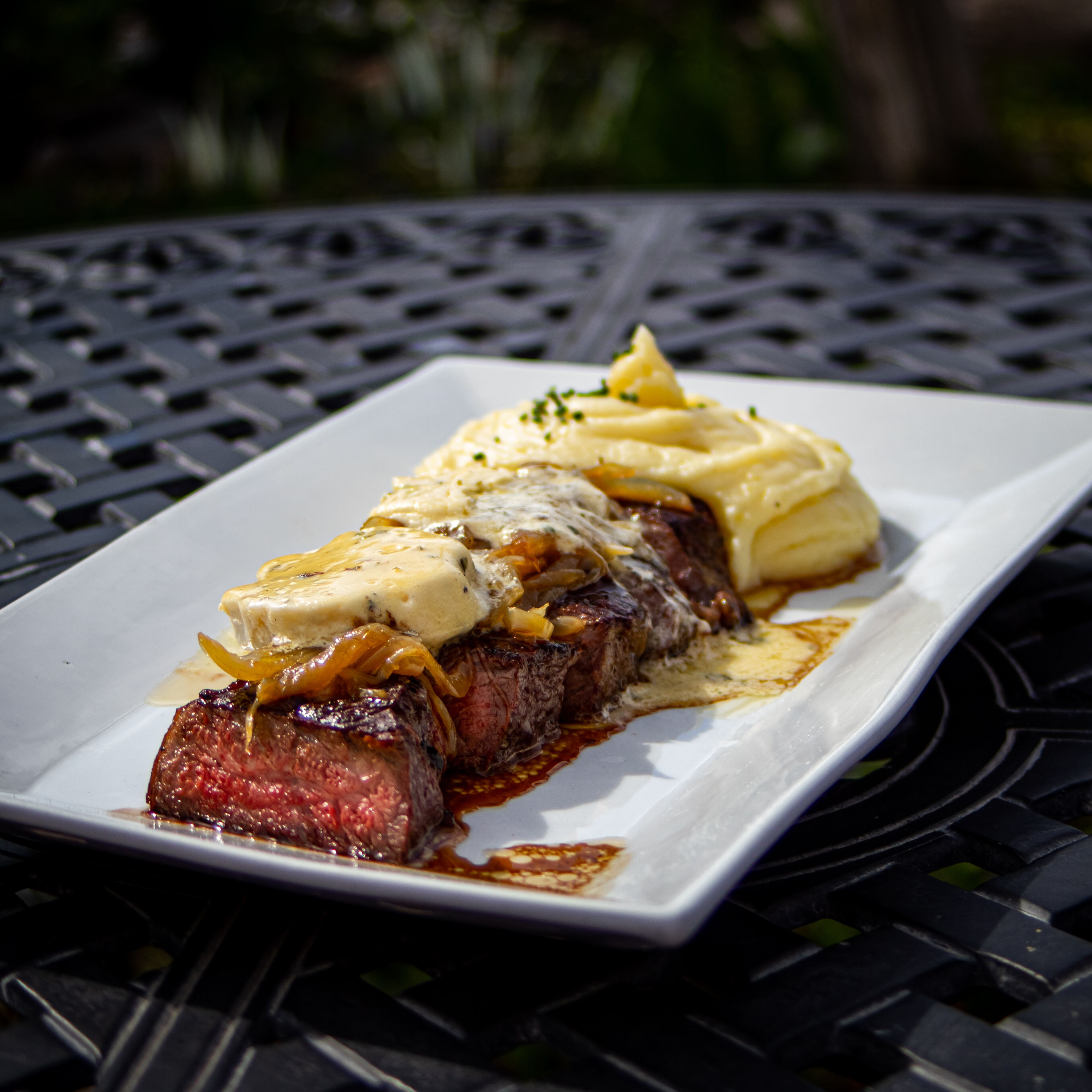 A steak with sauce and a side of mashed potatoes on a white plate.