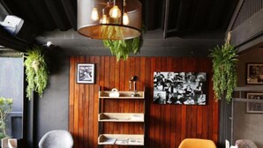 A cozy restaurant interior with wooden panel walls, a central shelf with books and decorative items, hanging plants, and a black and white photo collage. - Baan Kamala Fantasea Hotel (Kamala)