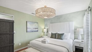 Une chambre à coucher avec un lit, des tables de chevet, un banc, un lustre et un tableau au mur.