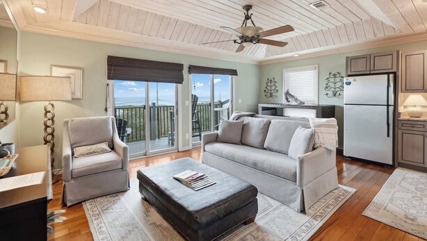 Un vaste espace de vie comprenant un canapé, des fauteuils et une table basse. Il y a également un balcon avec vue, un coin cuisine et un ventilateur de plafond.