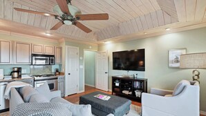 Un vaste espace de vie comprenant une cuisine, un ventilateur de plafond, un téléviseur à écran plat et un coin salon confortable.