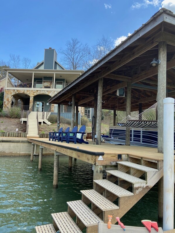 A dock extending into a body of water with wooden steps leading up to a covered seating area with blue chairs.