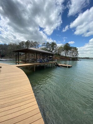 A wooden dock extending into a calm lake, with a covered seating area and a small pavilion.